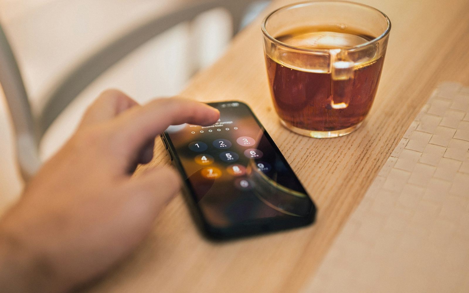 Bàn tay kiểm tra điện thoại có màn hình khóa cạnh ly cà phê