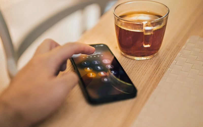 Bàn tay kiểm tra điện thoại có màn hình khóa cạnh ly cà phê