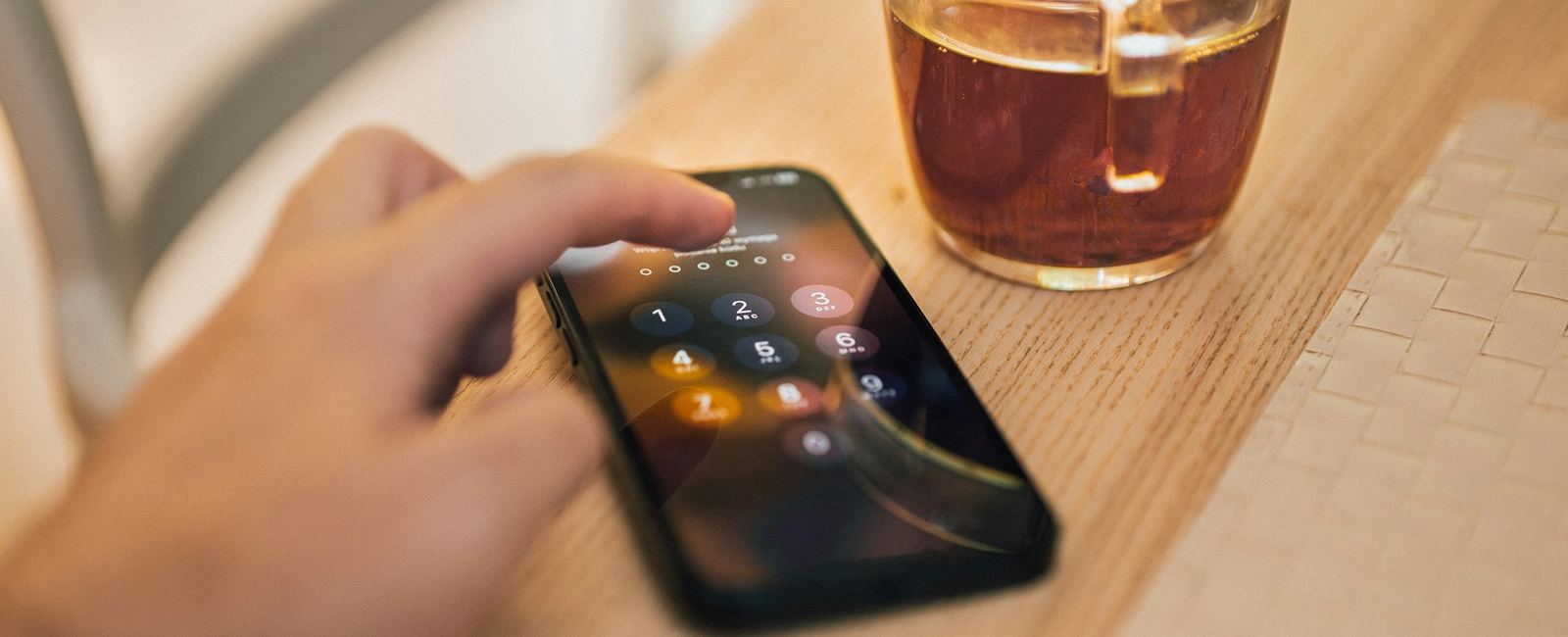 Bàn tay kiểm tra điện thoại có màn hình khóa cạnh ly cà phê