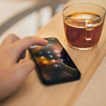 Bàn tay kiểm tra điện thoại có màn hình khóa cạnh ly cà phê